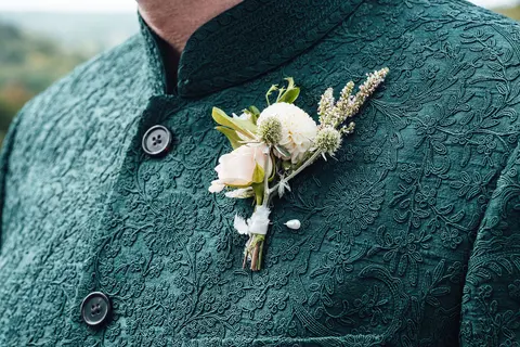 A rose and grass buttonhole on a green embroidered jacket