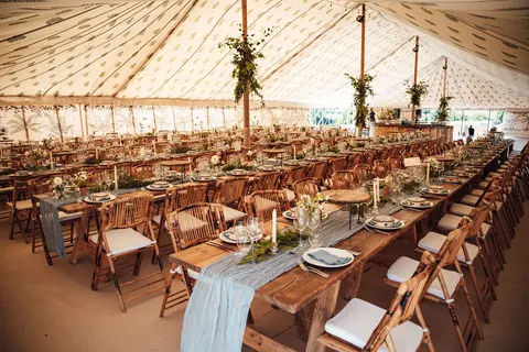 Long wooden tables laid for dinner inside a marquee