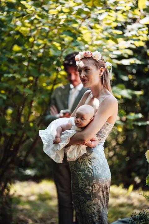 A guest in a flower crown holding a baby among the trees