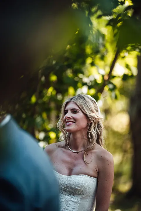 The bride smiling in dappled light during the ceremony
