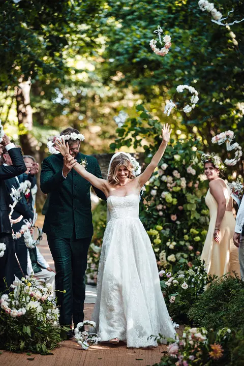 The couple walking back down the aisle with their arms raised as guests cheer