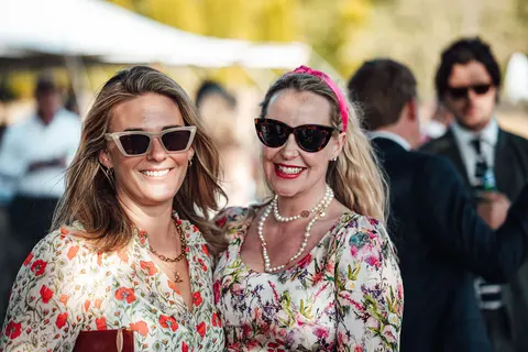 Two guests in sunglasses and floral dresses smiling at the camera