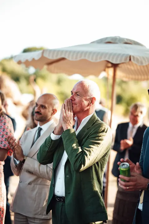 A guest in a green blazer clapping under a parasol