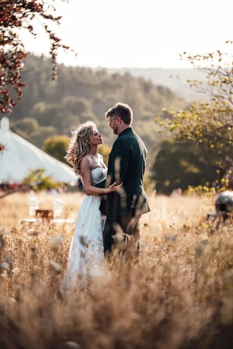 The couple standing together in a meadow with hills behind