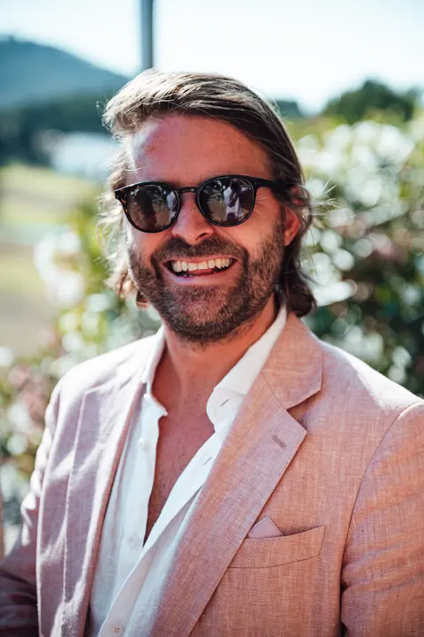 A guest in a pink linen suit and sunglasses smiling