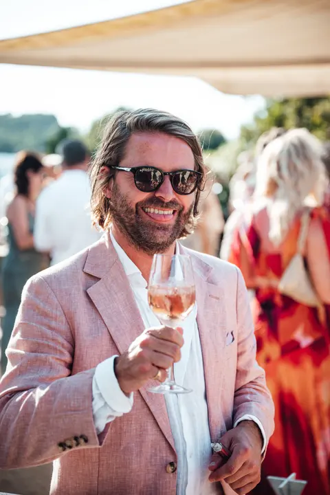 A guest in a pink jacket raising a glass of rosé