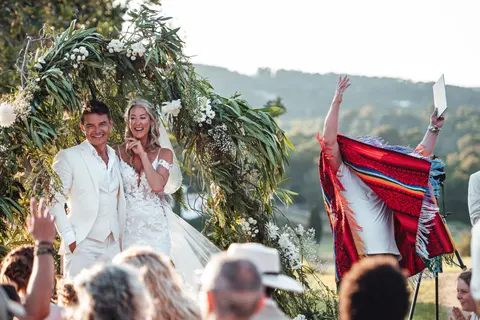 The couple under an arch of olive branches as a guest cheers