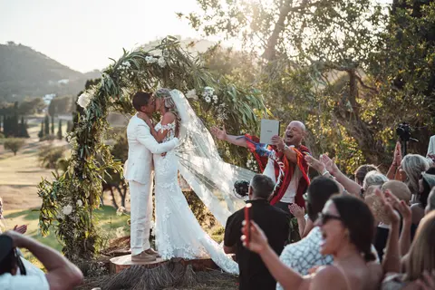 The couple kissing under the olive arch while guests applaud