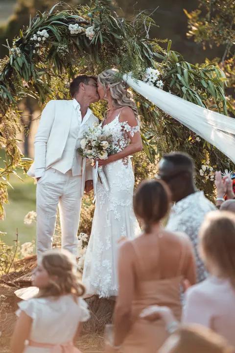 The couple kissing under the arch as a flower girl watches