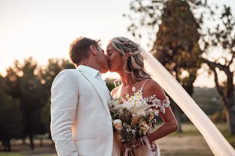 The couple kissing among the trees, her veil trailing