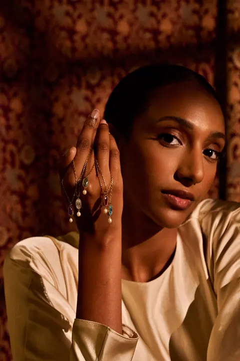 Model holding five gold pendant necklaces with coloured stones and pearls draped over her hand