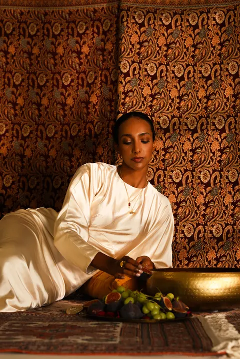Model in ivory silk leaning over the brass bowl of fruit