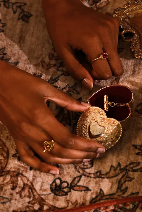 Hands opening a small heart shaped jewellery box on a carpet