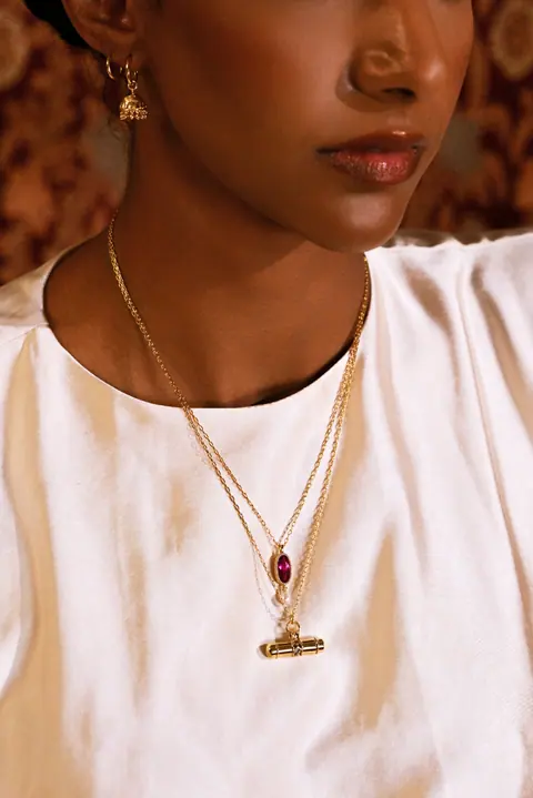 Close portrait with a gold chain and garnet pendant over ivory silk