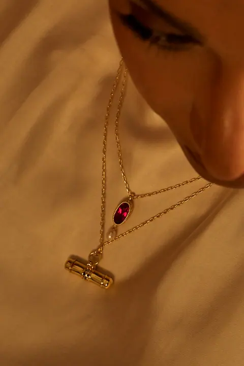 Gold T bar necklace with a garnet drop resting on ivory silk