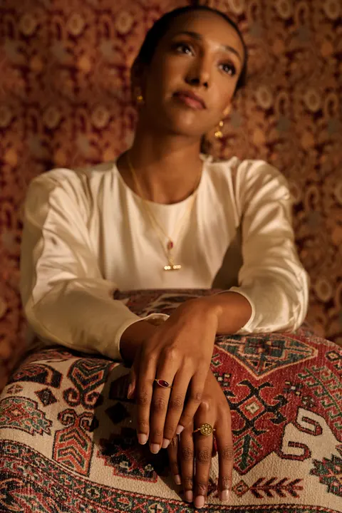 Model seated with her hands resting on a cushion