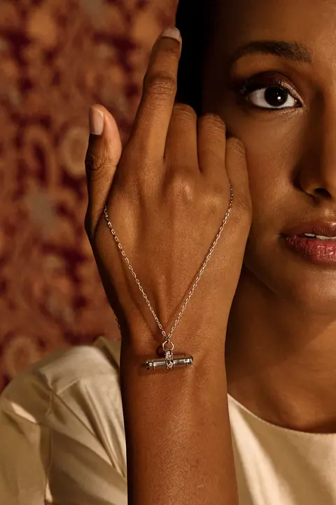 Hand raised to the face wearing a fine gold bracelet chain