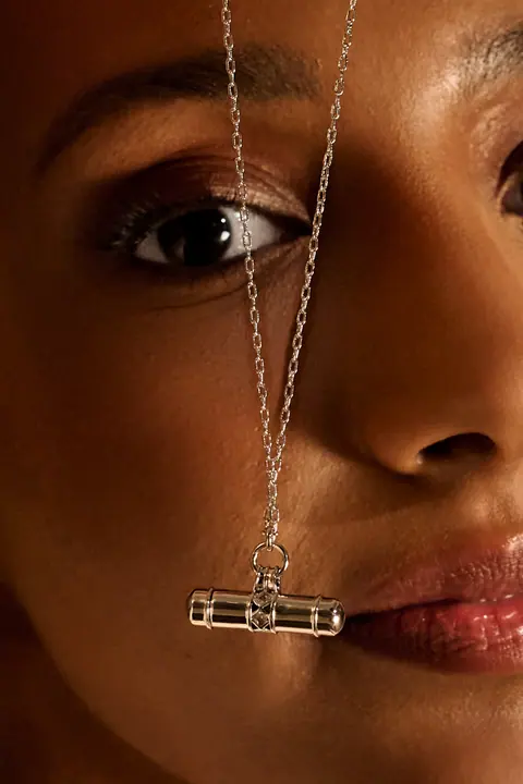 Close up of a gold chain with a T bar pendant held across the face