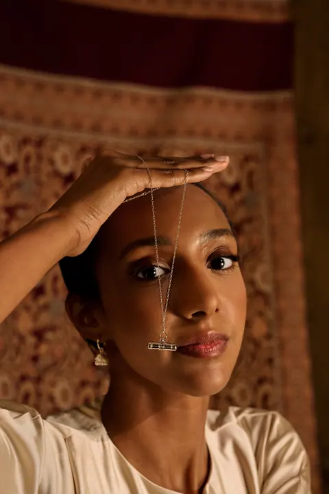 Model with her hand on her head and a gold chain hanging across her face