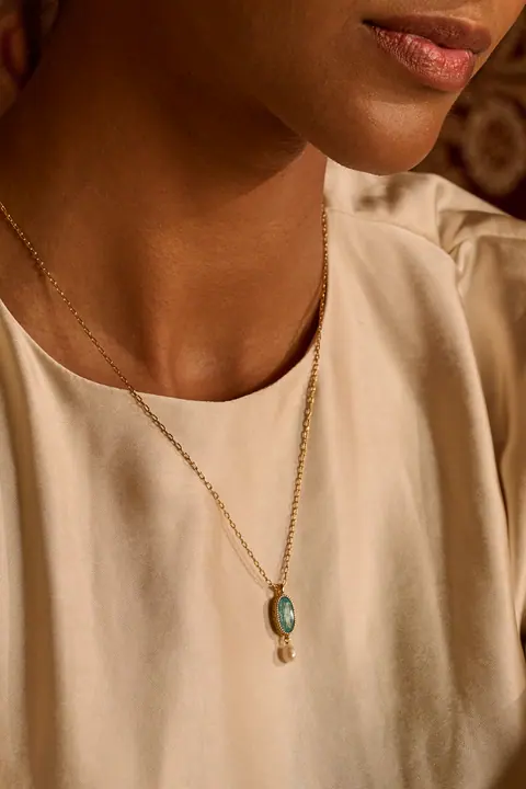 Gold pendant with a green stone and pearl drop over ivory silk