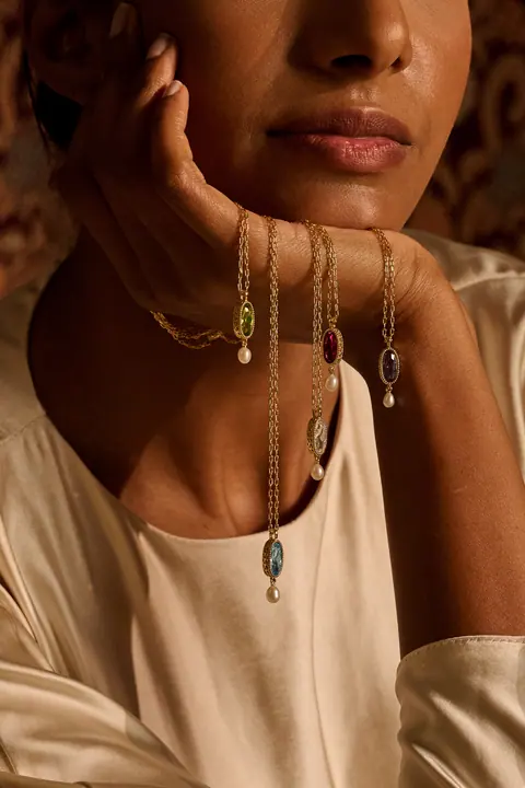 Several gold pendants with coloured stones looped over the model's wrist