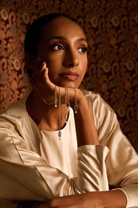 Layered gold bracelets on the model's wrist, hand at her cheek