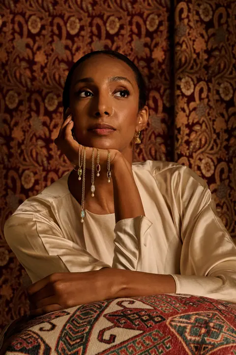 Model seated with her chin on her hand, pendants draped over her wrist