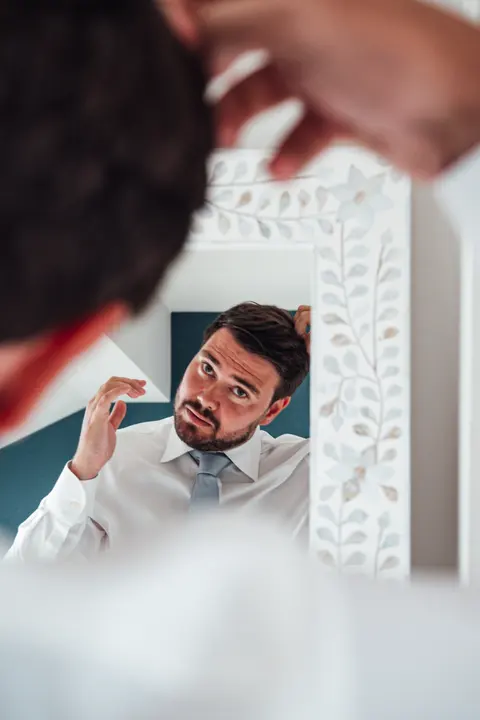 The groom fixing his hair in a mirror