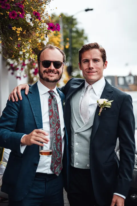 The groom and a friend in suits outside a pub