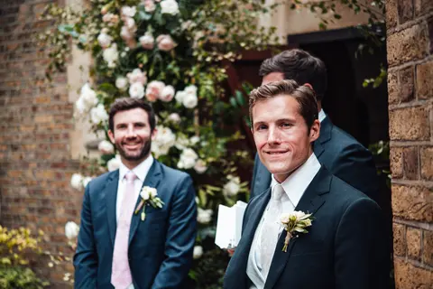 Two groomsmen by a doorway of climbing roses