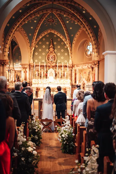 The bride walking down a flower lined aisle towards a gilded altar