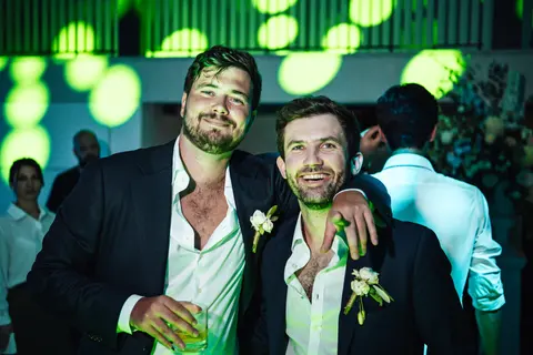 Two guests with their arms around each other under green lights