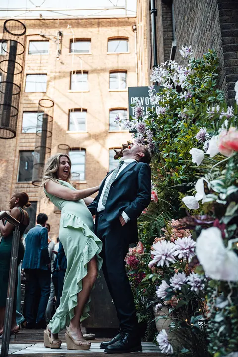 Two guests posing on the steps between banks of flowers
