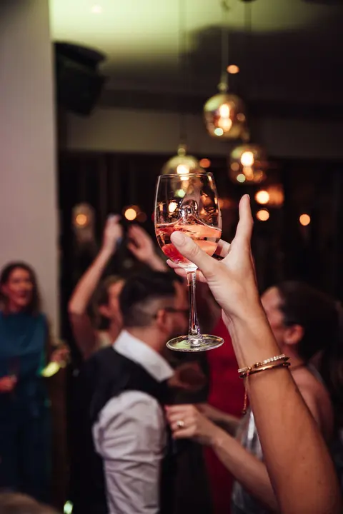 A hand raising a wine glass above the dance floor