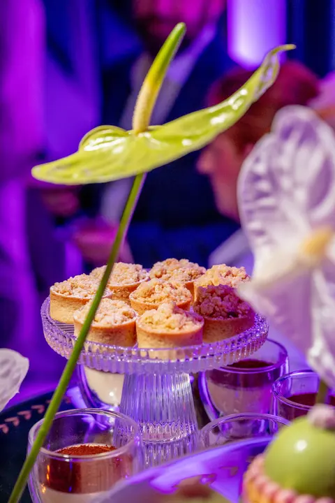 A dessert stand lit purple with an anthurium in the foreground