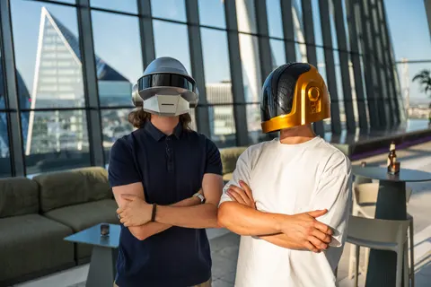 The two helmeted DJs standing with arms folded beside a window