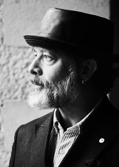 Black and white profile portrait of a bearded guest in a flat cap