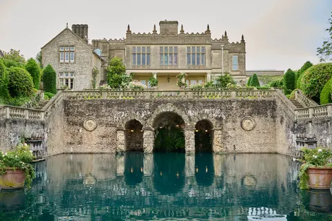 A stone country house above terraced gardens and a still pool