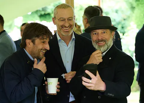 Three guests talking under the marquee, one in a hat