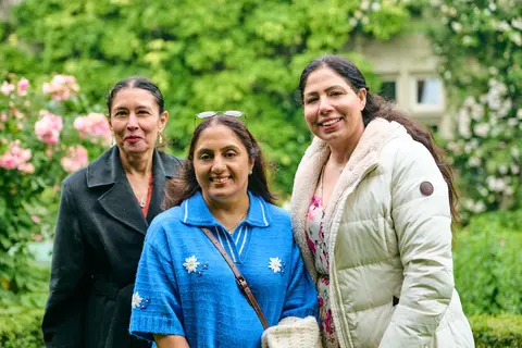 Three women in the garden, one in a blue top and headscarf
