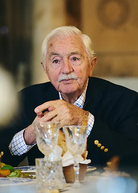 An older guest at the table, hands clasped, in colour
