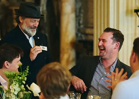 A guest in a hat sharing a card trick with the table