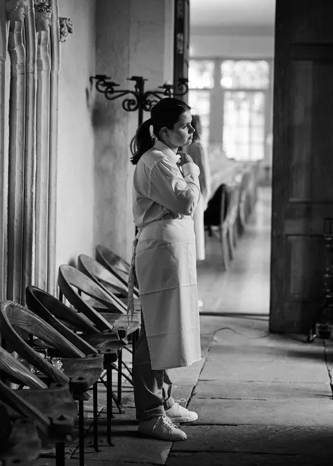 A woman in a long coat in a stone colonnade
