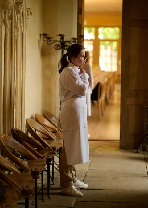 A woman in a long coat in a stone colonnade