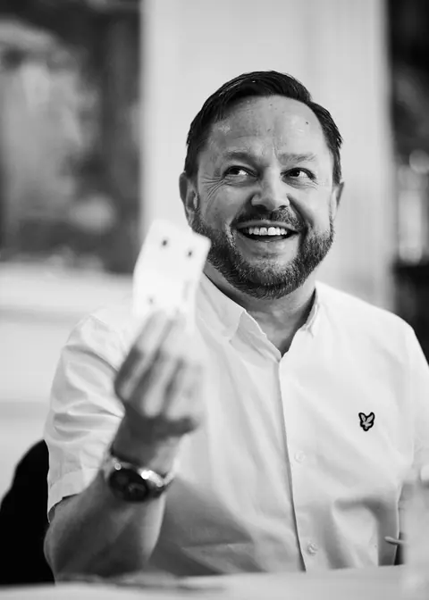 Black and white portrait of a guest holding up a playing card and grinning