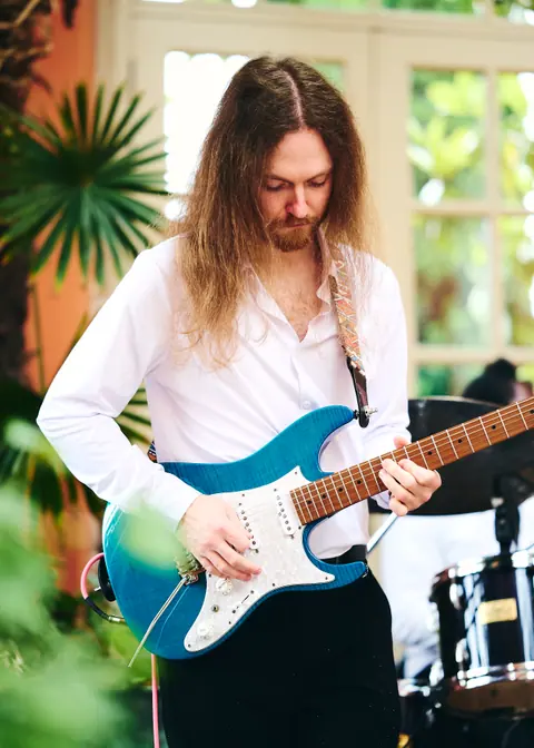 A guitarist with long hair playing a blue electric guitar